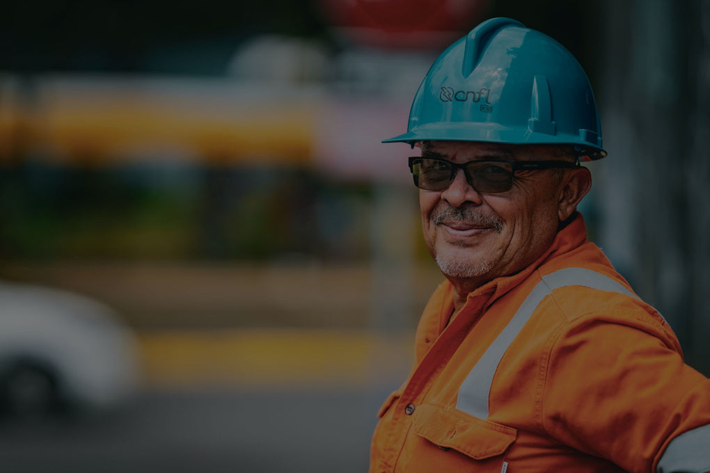 Trabajador con casco de seguridad y uniforme de alta visibilidad sonriendo en el lugar de trabajo.