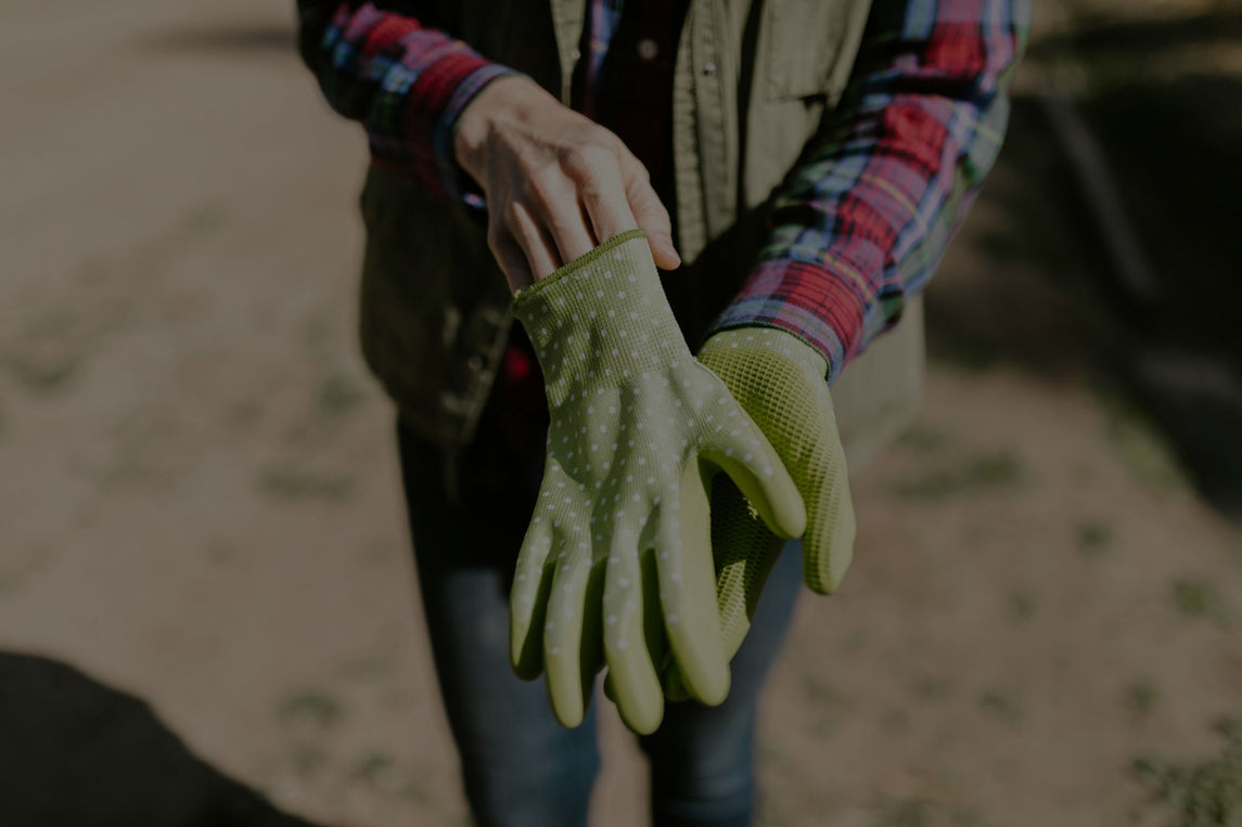 Persona colocándose guantes de seguridad de jardinería de color verde con puntos blancos, ideal para protección en tareas al aire libre.