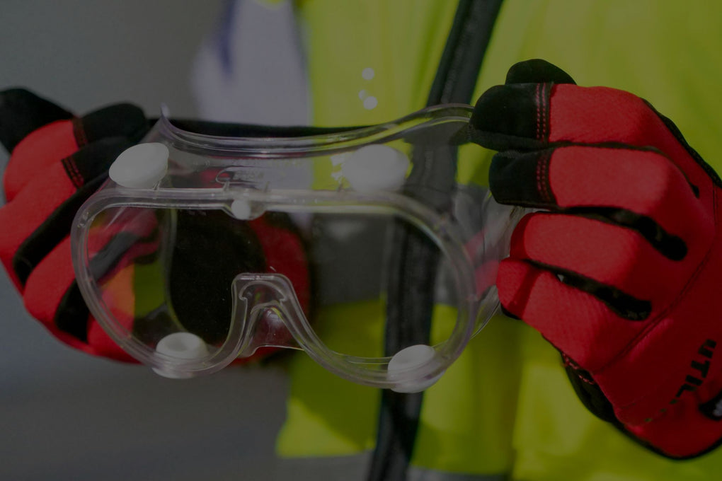 Trabajador sosteniendo gafas de protección ocular con guantes de seguridad rojos, resaltando la importancia de la protección visual en entornos laborales