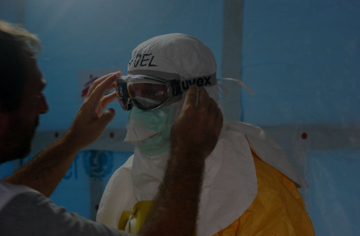 Profesional ajustando equipo de protección individual (EPI) en un trabajador, incluyendo gafas de seguridad y traje de protección, en un entorno sanitario o de riesgo biológico.