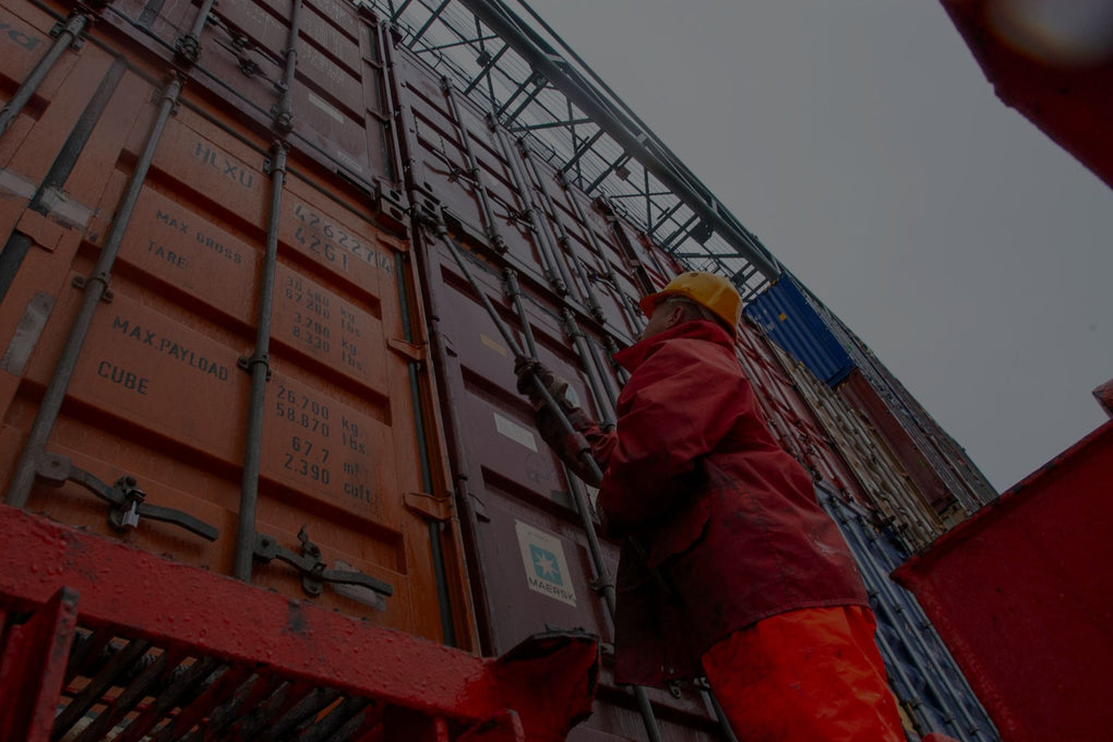 Trabajador con casco y ropa impermeable manejando contenedores en condiciones climáticas adversas